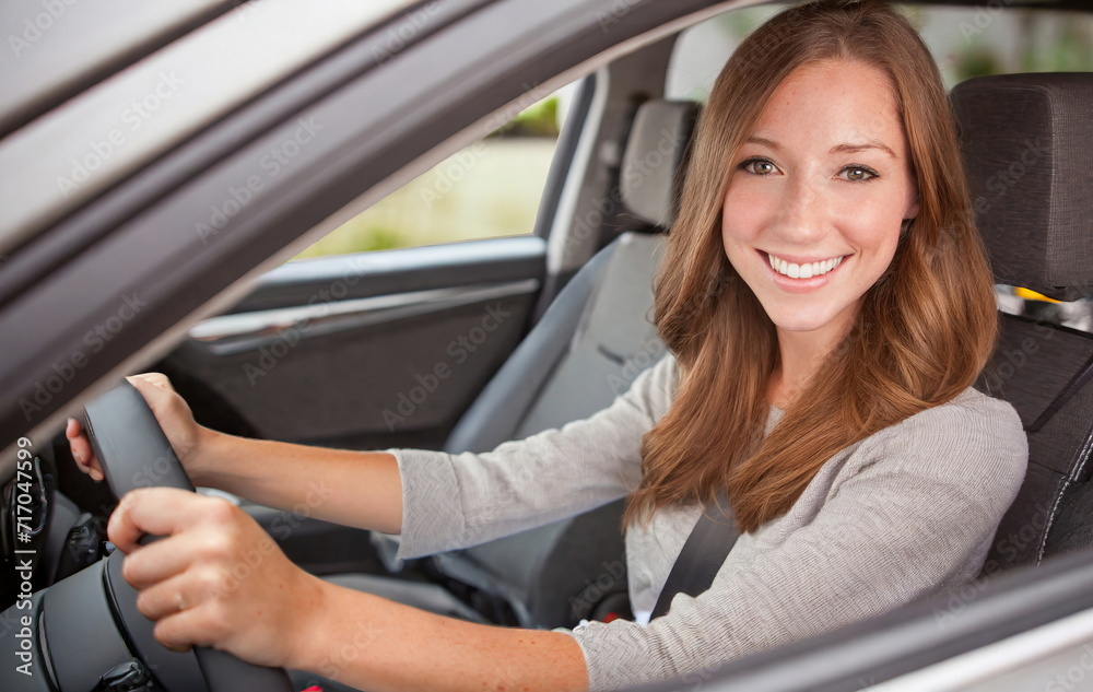 young adult woman driving a car, smiling joyfully, hands on steering wheel
