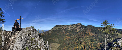 Wanderer (männlich) sitzt am Gipfelkreuz am Großen Rechenberg, Chiemgau, Alpen, Bayern, Deutschland