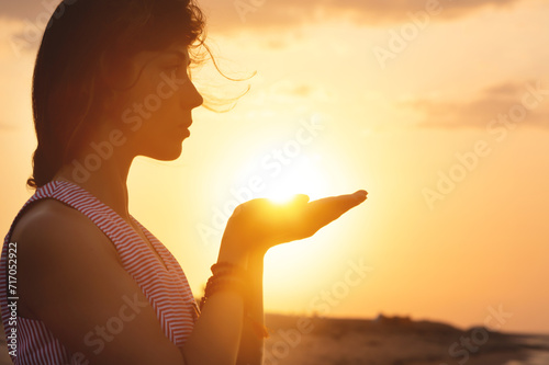 Portrait of a young woman in the form of a silhouette and hands holding the sun. Sunset over the sea, the sun on the palms of a calm girl