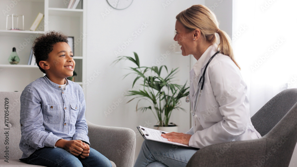 Fototapeta premium Happy female doctor giving high five to cute little African American boy patient at hospital consultation. A smiling pediatrician will cheer up a small child at the clinic. Healthcare concept.