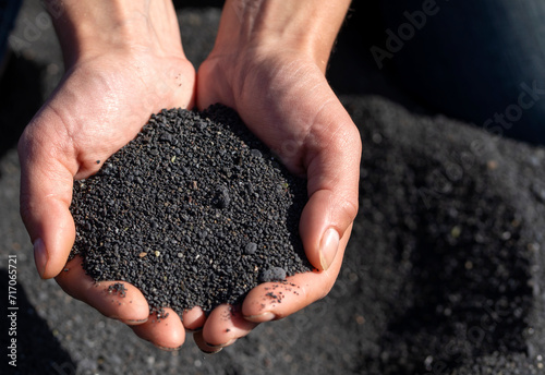 A person is holding a black volcanic sand in his or her hands, closeup view.
