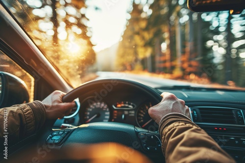 man with his hands on the steering wheel against the background of a forest at bright sunset, visible through the windshield photo