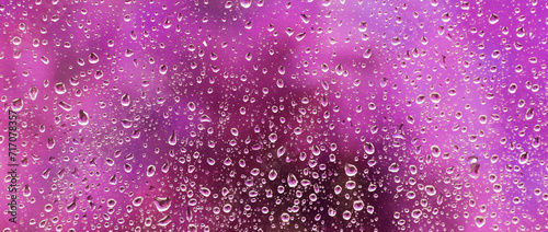 Beautiful colored drops on glass from rain on a blurred purple background. Panorama.