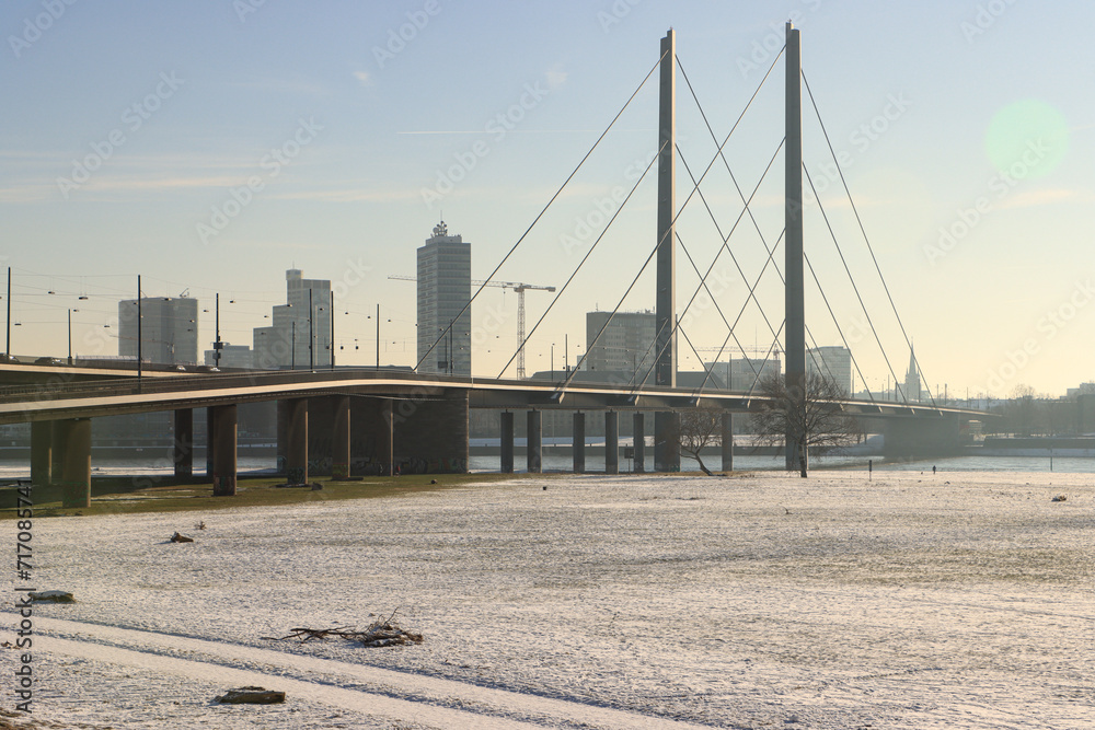 Fototapeta premium Winterliches Düsseldorfer Rheinufer; Blick von Oberkassel auf die Rheinkniebrücke und Skyline der Stadt