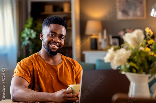 Young African American man sitting at home using laptop for video call.