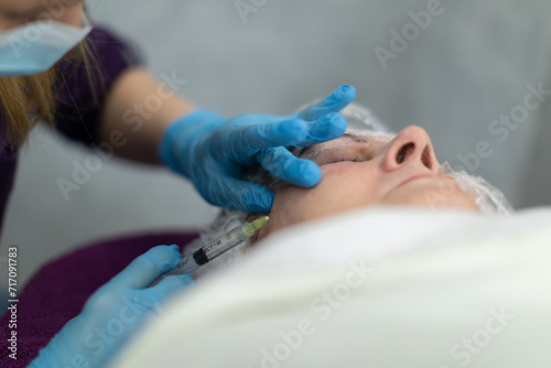 The beautician performs a series of small injections on the client's face.