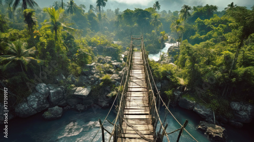 Suspension wood bridge in jungle, vintage dangerous footbridge across tropical river. Landscape of green forest and blue water. Concept of travel, adventure, nature photo