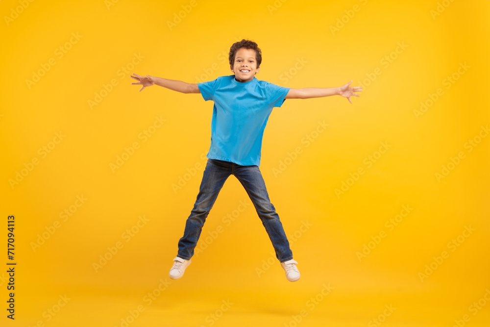 Joyful boy jumping with arms outstretched, yellow backdrop