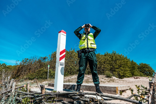 Immigration control officer surveying the coast with binoculars, vigilant in national border protection duties on a sunny day photo