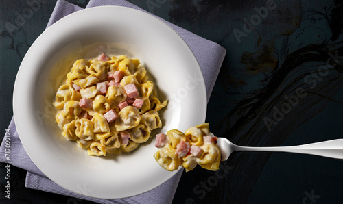 White soup plate and fork with tortellini with cream and ham on black background photo