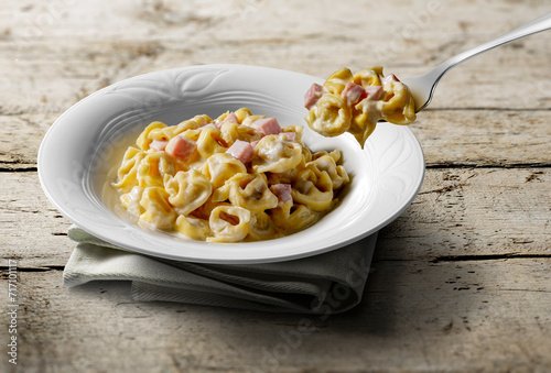 Tortellini soup plate and fork with cream and ham on wooden table