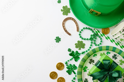 Shamrock soiree: An elegant St. Paddy's affair. Top view of paper plate, cutlery, cups, straws, hat, horseshoe, gift, trefoils, coins, confetti, beads on white background with space for greetings