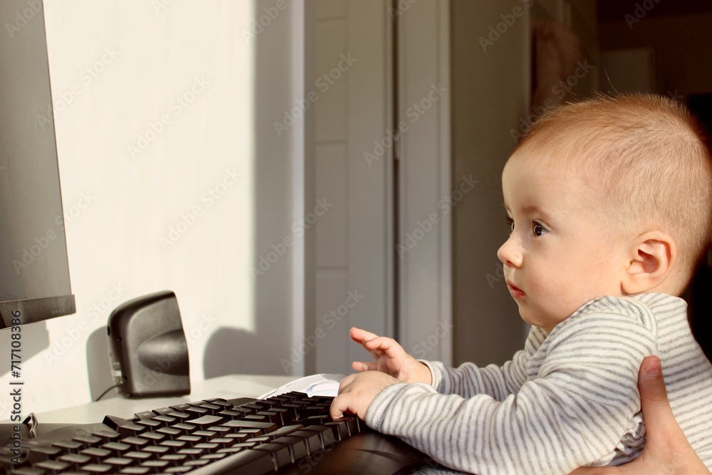 child playing with computer, A cute baby boy is sitting at the computer and looks attentively with admiration child playing with computer, A cute baby boy is sitting at the computer and looks attentively with admiration