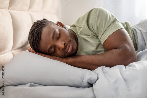 african guy asleep resting head on hands lying in bed photo