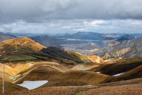 View at volcanic mountains with snow, green moss on hills and black lava on Icelandic highlands at Landmannalaugar, Iceland. Famous Laugavegur hiking trail with dramatic sky