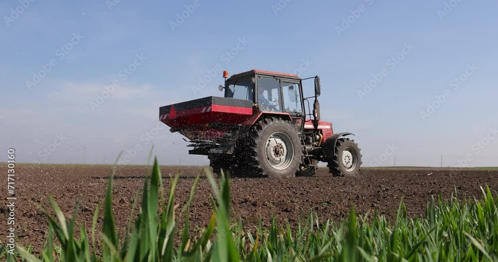 Farmer with agricultural machinery fertilizing agricultural field in spring time, green wheat in the foreground, slow motion. Spreading mineral fertilizer, cinematic low angle gimbal shot Farmer with agricultural machinery fertilizing agricultural field in spring time, green wheat in the foreground, slow motion. Spreading mineral fertilizer, cinematic low angle gimbal shot