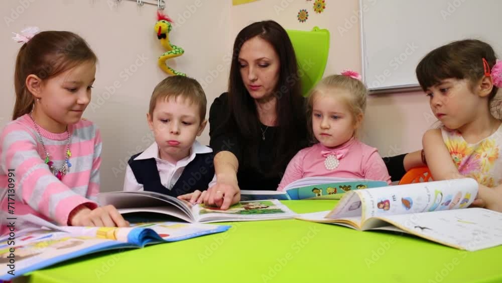 A teacher and children look at a textbook, teacher points in the book A teacher and children look at a textbook, teacher points in the book