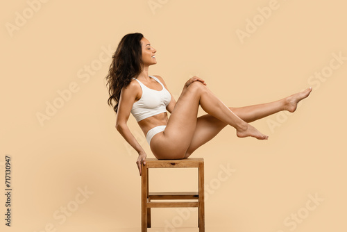 Energetic young woman in white underwear posing on chair against beige background