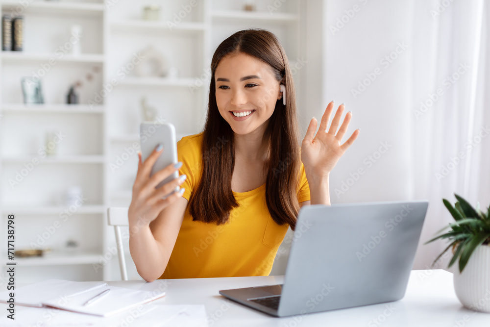 Asian Woman Making Video Call On Smartphone While Sitting In Home Office Asian Woman Making Video Call On Smartphone While Sitting In Home Office