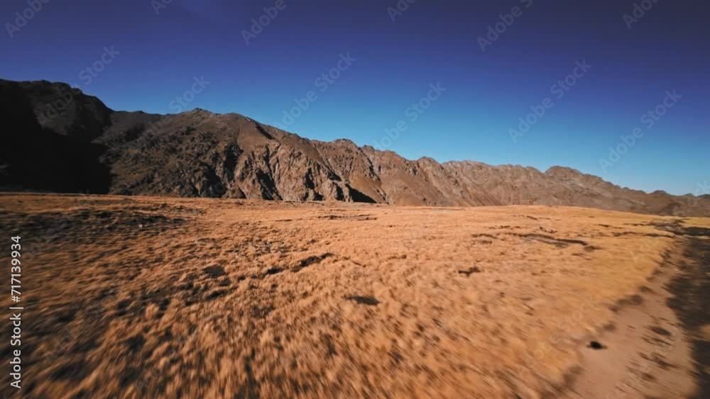 Low flight of a sports FPV drone at high speed high in the mountains over a yellow autumn field surrounded by snow-capped mountains of the Caucasus mountain range and Elbrus volcano Low flight of a sports FPV drone at high speed high in the mountains over a yellow autumn field surrounded by snow-capped mountains of the Caucasus mountain range and Elbrus volcano
