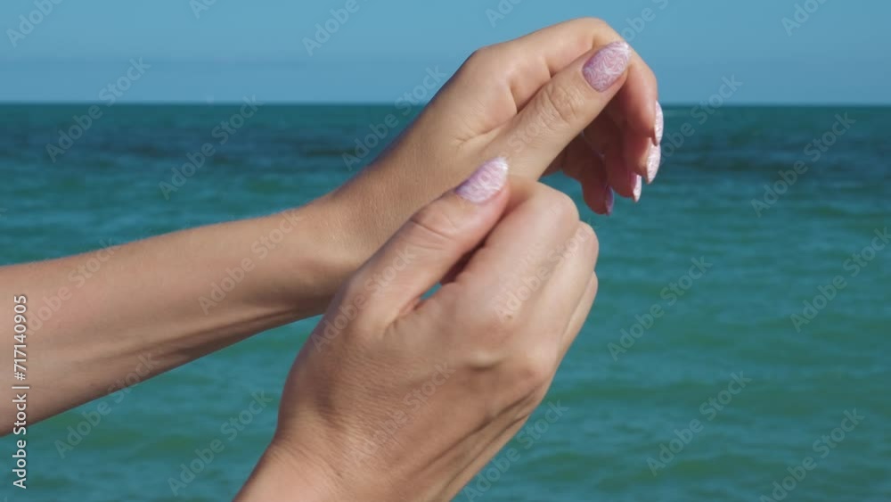 Female hands with beautiful natural pink elegant manicure. Mediterranean sea on the background. Spa concept. 