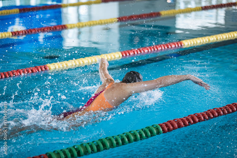 Successful professional female swimmer swimming butterfly stroke in the indoor lap pool, front view. Concept of determination and hard sports training.