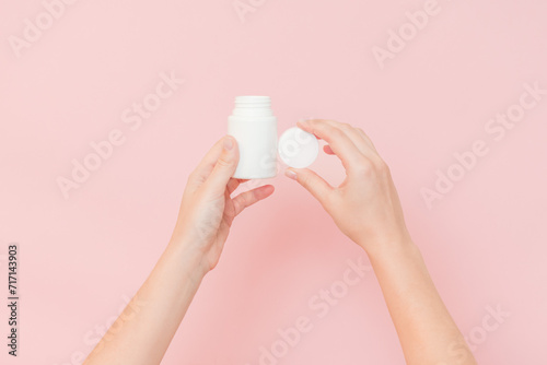 White bottle plastic tube in woman s hands on pink background. Packaging for pills  capsules or supplements. Cosmetics