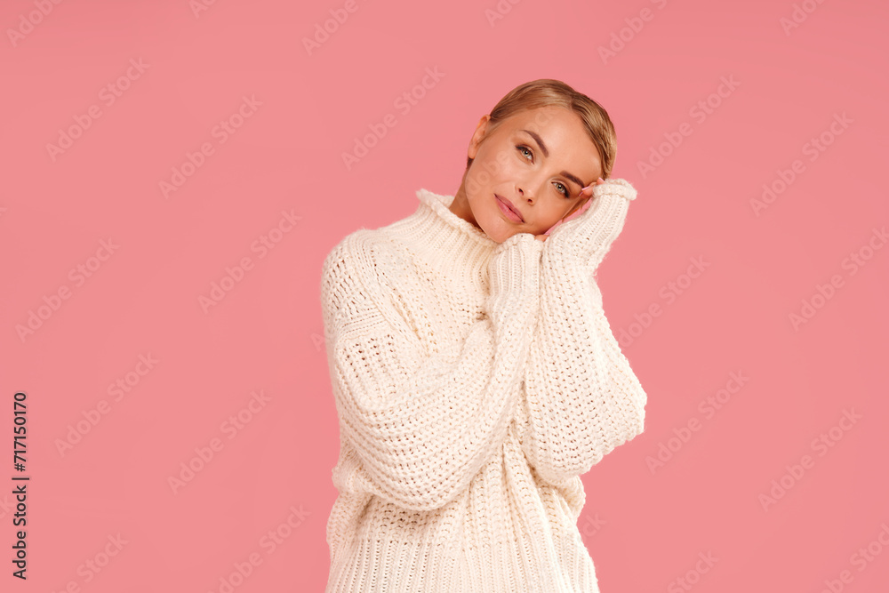 Portrait of happy young woman with blonde short hair wearing warm wool sweater, looking at the camera. A lot of copy space on pink pastel studio background. Portrait of happy young woman with blonde short hair wearing warm wool sweater, looking at the camera. A lot of copy space on pink pastel studio background.