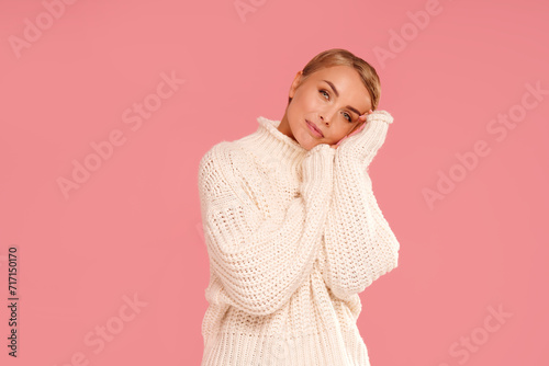 Portrait of happy young woman with blonde short hair wearing warm wool sweater, looking at the camera. A lot of copy space on pink pastel studio background.