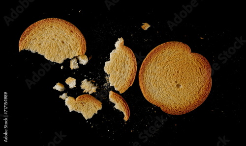 Broken round bread rusks with crumbs, whole wheat toast slices isolated on black background, top view