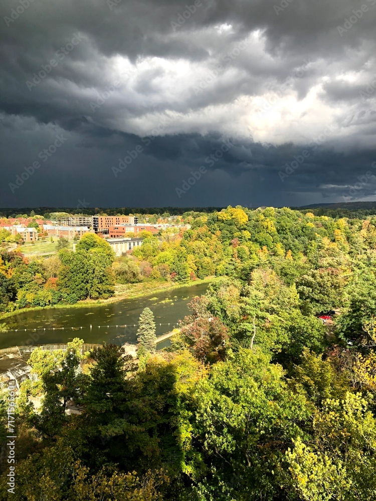 Trees and river in sunshine with dark clouds above