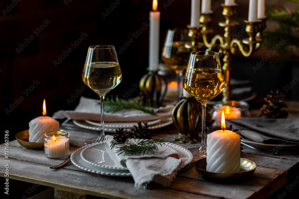 Rustic elegant table decor for christmas family dinner. Center piece with white candle, pine cone, fir tree branches. Zero waste eco-friendly home decoration. Cozy atmosphere, wooden background.