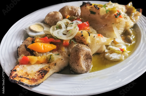 View of a typical Portuguese dish, named Bacalhau à Lagareiro, grilled cod fish, potato, egg, onions, green and red peppers and garlic, with olive oil, black background