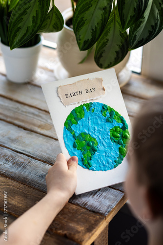 Concept of raising awareness about the environmental issues on the Earth day. Kid doing craft postcard with planet on it. Promoting sustainable lifestyle, conscious consumption, environment protection