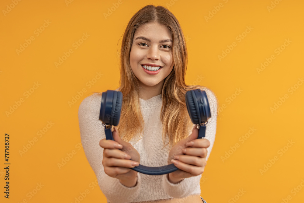 A woman smiling holding blue headphones towards camera A woman smiling holding blue headphones towards camera