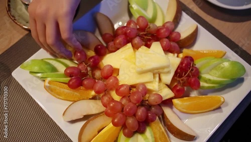Close-up of female hand taking slice of orange from plate of fruit