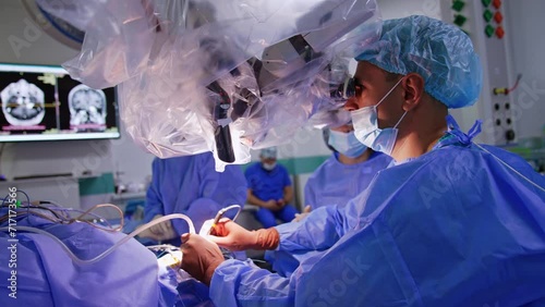 Confident male surgeon looks at binoculars of microscope covered with plastic. Doctor performs neurosurgical procedure on brain. photo