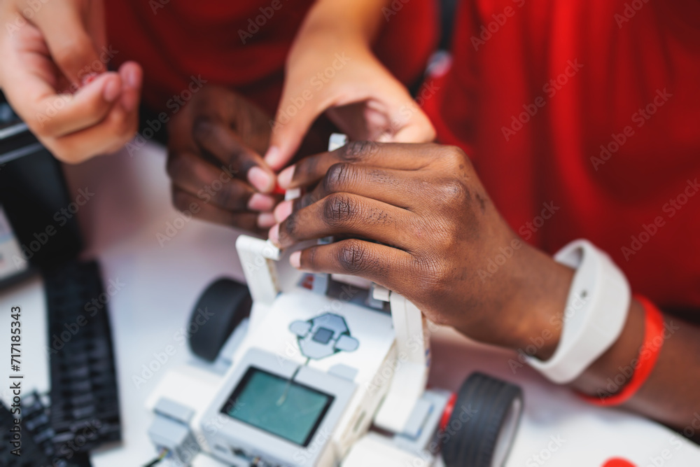 Group of diverse children kids with robotic vehicle model, close-up view on hands, science and engineering lesson in a classroom, making, coding and programming a robot in a school, robotics projects