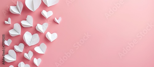 Valentine's Day banner with white paper hearts on a pink background viewed from above. © TheWaterMeloonProjec