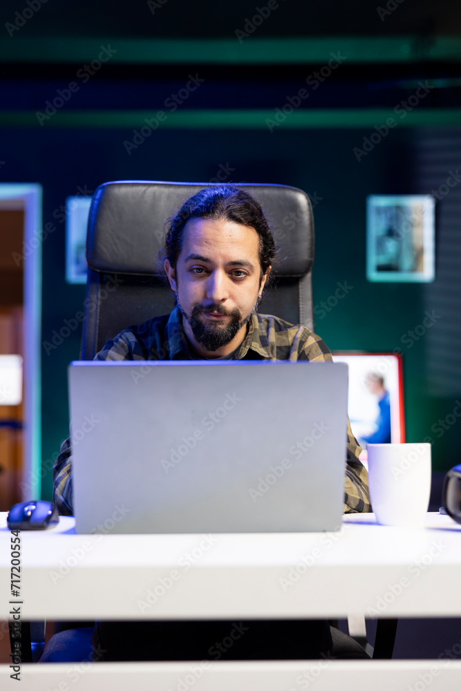 Young male freelancer sitting and working from home, utilizing his laptop for online research. Dedicated college student studying online, using modern technology to review information on internet.