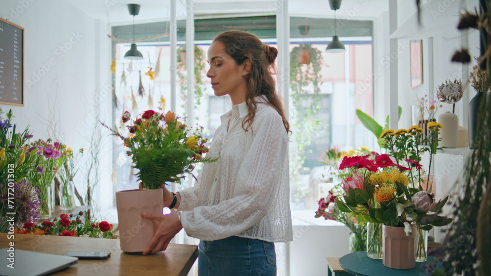 Beautiful florist look camera at flower workplace job. Joyful girl work in shop.