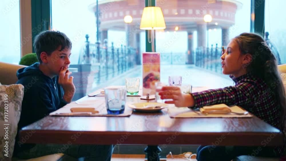 Boy and girl sit in cafe and wait for dishes. Rotunda behind window Boy and girl sit in cafe and wait for dishes. Rotunda behind window