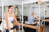 Positive concentrated young girl practicing pilates stretching exercises on reformer at gym