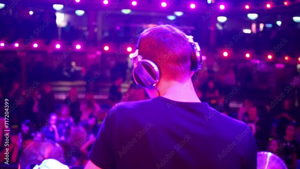 Back view of DJ is standing on a stage in dance club. Back view of DJ is standing on a stage in dance club.