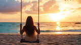 A young women with long hair is sitting on a swing set on the ocean shore. Sandy beach at sunset.