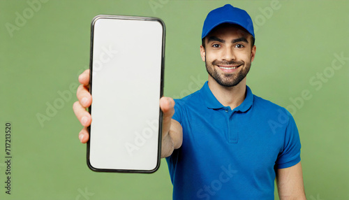 Full body delivery guy employee man wears blue cap t-shirt uniform workwear work as dealer courier big huge blank screen mobile cell phone hold box isolated on plain green background. Service concept photo