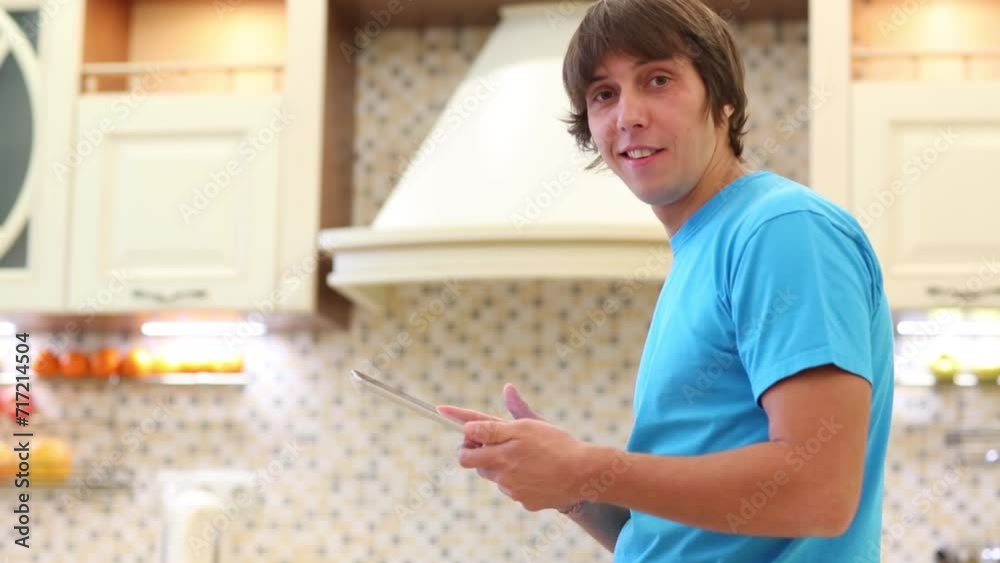 The man looks at tablet, into the camera and back at the kitchen