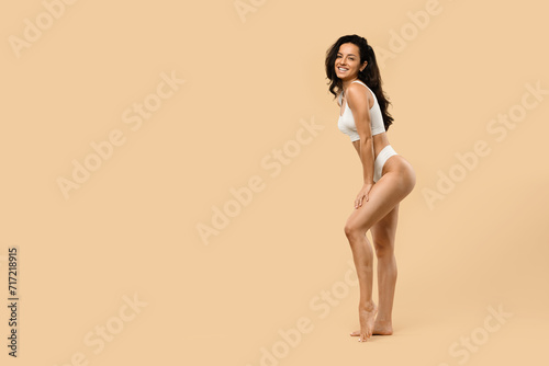 Smiling beautiful woman with sculpted figure posing in lingerie against beige background