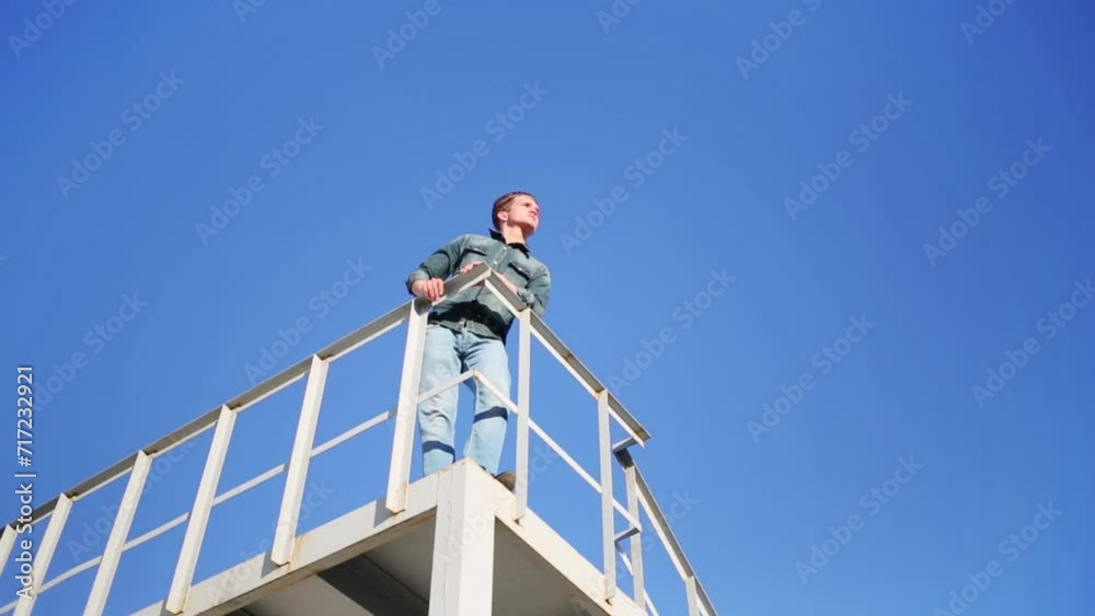 Man in denim trousers and shirt standing at railing on roof on sky. Man in denim trousers and shirt standing at railing on roof on sky.