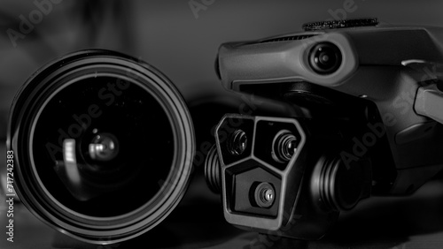 Black and white macro image with the front right angle of a drone with 3 camera gimbal, and a wide angle camera lens.